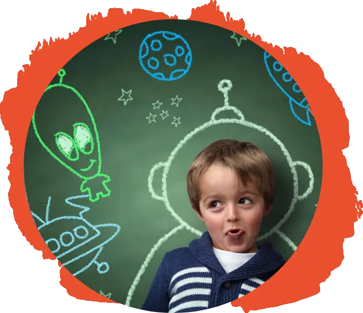 A boy is standing in front of a chalkboard with drawings on it.