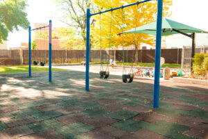 A playground with swings and a green umbrella.