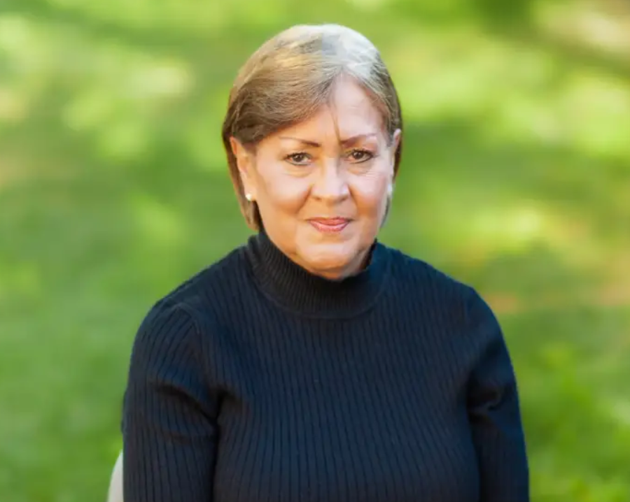 A woman in black sweater standing outside near trees.
